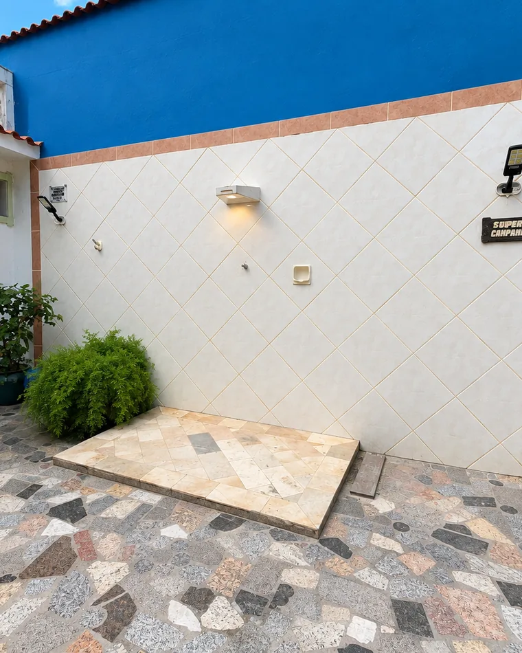 Pátio externo com piso de pedra em mosaico, parede azul e área de serviço ao fundo