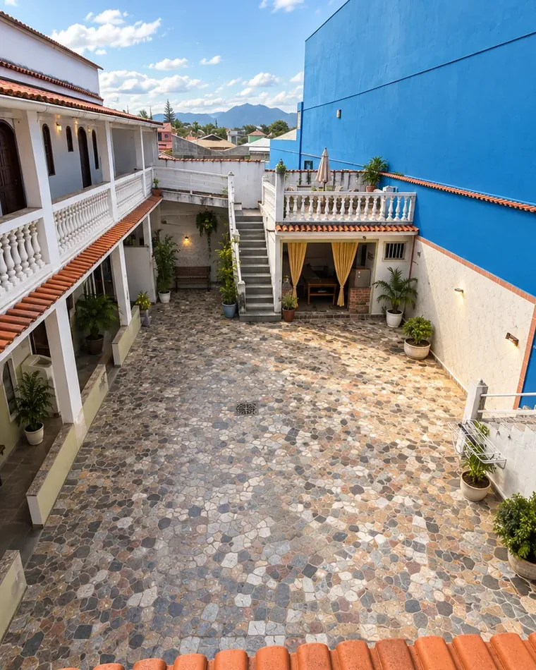 Pátio interno da pousada com piso de pedra, varandas com balaústres brancos e muro azul sob céu limpo