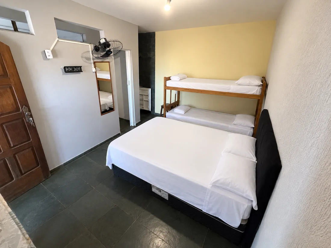Suíte com cama de casal e beliche de madeira, com ventilador e espelho na parede
